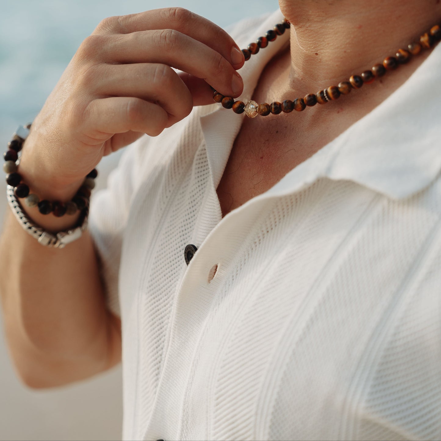 Man wearing a beaded necklace and bracelet by the ocean